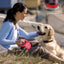 Woman sitting with a dog on grass, holding a red flexi retractable leash.