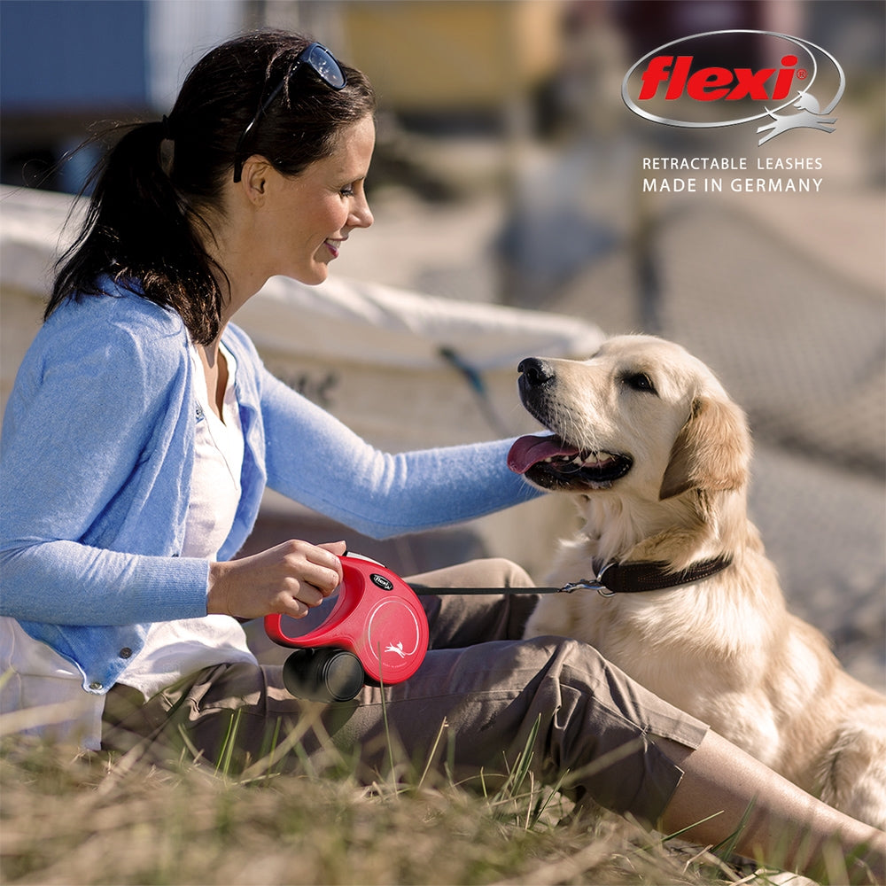 Woman sitting with a dog on grass, holding a red flexi retractable leash.