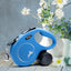 Blue retractable dog leash with a brand logo on a wooden surface with flowers in the background