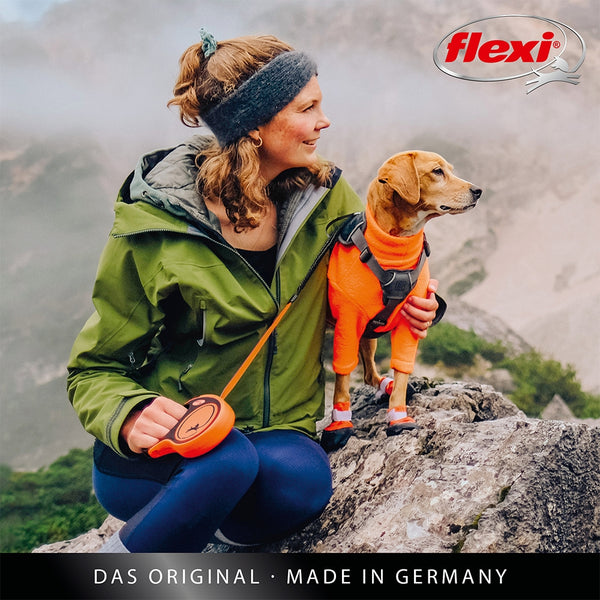 Woman with a dog in an orange jacket on a mountain, Flexi brand visible