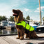 Dog wearing a bright yellow life jacket on a dock with boats in the background