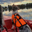 Dog wearing an orange life jacket on a boat during sunset.